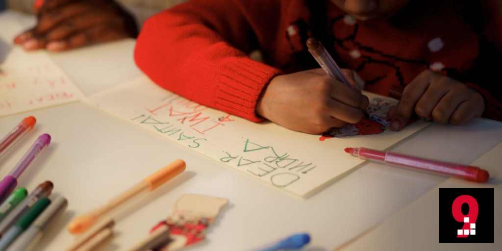 Kinderhand (roter Pulli-Ärmel zu sehen) schreibt mit Holzstift einen Wunschzettel Dear Santa .... Rote 9, Geek Space 9 Logo.